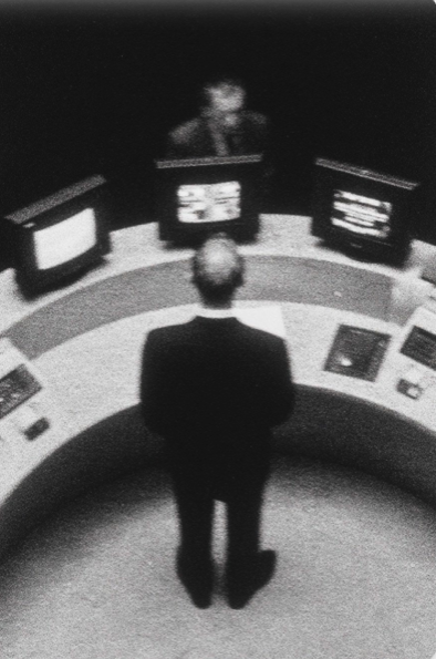 Foto en blanco y negro de un hombre de traje frente a una consola curva de monitores